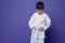 Horizontal portrait of a confident teenage boy aikido wrestler tying white belt of his kimono,  over violet background
