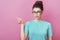 Horizontal portrait of elegance woman with hair bun and glasses, pointing on copy space with finger isolated over pink background.