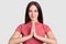 Horizontal portrait of faithful brunette young woman keeps plams in praying gesture, dressed casually, poses against white backgro