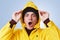 Horizontal portrait of stunned stupefied man wears yellow raincoat, hood and hat, looks out of window, sees heavy rain outside, sh