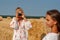 Horizontal portrait of two happy friendly sisters in embroidered shirts who photograph each other against a background of a mown