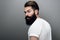 Horizontal rear view of brutal handsome young bearded male model looking at the camera, posing on a gray studio background.