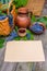 Horizontal sheet of paper lay beside basket,bowl with grapes, jar and cup with wine on rustic wood.