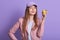 Horizontal shot of charismatic tender fair haired female holding apple in one hand, sticking to healthy lifestyle, having peaceful