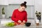 Horizontal shot of European woman waits for baby, cuts tomatoes, makes fresh salad, uses knife, poses against kitchen interior,