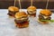 Horizontal shot of four mini burgers with cheese, lettuce, tomato and bacon on a table