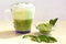 Horizontal shot of Green tea matcha latte with milk foam in a cup with green leaves and powed matcha.