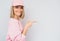 Horizontal shot of happy casually dressed in pink with cap Caucasian blonde female smiling and  indicating something on white wall