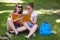 Horizontal shot of happy female studens feels relaxed while sit crossed legs on green grass, enjoy spring weather, have positive e