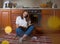 Horizontal shot of a happy woman sitting on the floor in the kitchen with an open notepad waiting for a delicious pie