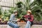 Horizontal shot of lovely elderly couple man and woman, gardeners, wearing hats and casual shirts, sitting in greenhouse