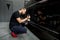 Horizontal shot of man auto service worker, wearing black clothes, putting special polish wax or cream on the orbital