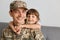 Horizontal shot of positive military man soldier wearing camouflage uniform and cap, posing with his daughter, looking at camera