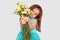 Horizontal shot of pretty dark haired female child in festive dress stretches hands with beautiful flowers, has appealing look,