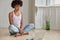 Horizontal shot of relaxed dark skinned woman sits in lotus pose, watches training video, learns yoga, dressed in