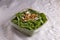 Horizontal shot of a salad with  greens, cheese and walnut in a plastic plate on a white tablecloth