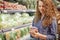 Horizontal shot of satisfied female buys food in supermarket, reads product information, chooses necessary product for preparing s