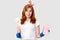 Horizontal shot of satisfied redhead female janitor holds brush and sponge, does spring cleaning, has positive expression,