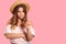 Horizontal shot of serious curious woman with long hair, dressed in fashionable straw hat and blouse, points with fore finger at