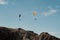 Horizontal shot of two paragliders gliding over a cliff