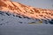 Horizontal shot of a yellow aircraft landing at the foot of snow covered mountains at sunset