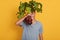 Horizontal shot of young handsome male holding bunch of beets in hand, hiding behind fresh vegetables, posing in casual outfit,