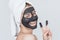 Horizontal studio portrait of happy young woman blink with eye with cosmetic black clay organic mask on her face, wears black