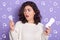 Horizontal studio shot of beautiful desperate young woman holding sanitary pad and menstrual cup in both hands, looking aside,