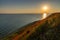 Horizontal view of beautiful ocean coast with sloping grassy hills and endless fields of poppies and a sun star