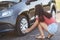 Horizontal view of experienced female driver tries to fix flat tire, uses special equipment, solves problem with wheel, poses on r