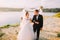 The horizontal view of the happy newlyweds walking arm in arm near the river.