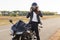 Horizontal view of stylish confident female biker dressed in fashionable clothes, sits on motorbike, wears helmet, covers long des