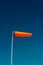 Horizontally flying orange windsock and clear dark blue sky.