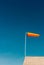 Horizontally flying orange windsock on metal rooftop and clear dark blue sky.