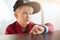 A horoizontal portrait of serious male child wearing trendy cap and red shirt having a smart watch on his wrist sitting at wooden