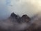 Horror mountain shadows. Dramatic fog among giant rocky mountains. Ghostly atmospheric view to big cliff in cloudy sky. Low clouds