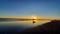 A horse-drawn carriage driving in far distance in front of the full sun at sunset time on a wet and reflecting beach sand