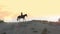 Horse riding. Equitation. Silhouette of horsewoman, riding a horse on towering sandy hill at sunset, in warm summer sun