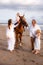 Horse riding. Little pretty girl on a horse. Father leading horse by its rein and talking to daughter. Wife stroking a horse.