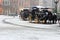 Horses carriage with old fashioned coach under snowfall on empty square in Europe. Winter travel background.