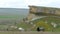 Horses graze on the field under the slopes of the cliff