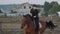 Horsewoman riding on brown horse and jumping the fence in sandy parkour riding arena. Competitive rider training jumping