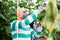 Horticulturist in medical mask harvesting cucumbers in hothouse