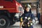 Hose in hands. Female firefighter in protective uniform standing near truck