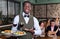 Hospitable African American waiter standing with serving tray, recommending dishes in restaurant