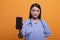 Hospital caregiver wearing medical instrument while holding mobile cellphone on orange background.