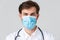 Hospital, healthcare workers, covid-19 treatment concept. Headshot of handsome determined doctor in medical mask, white