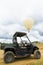 Hot air balloon flies in the sky over a four-by-four car standing on the field ground.