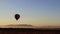 Hot Air Balloon slowly ascends over fog filled farm field and rolling hills at sunrise