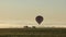 Hot Air Balloon slowly decends over fog filled farm field and rolling hills at sunrise